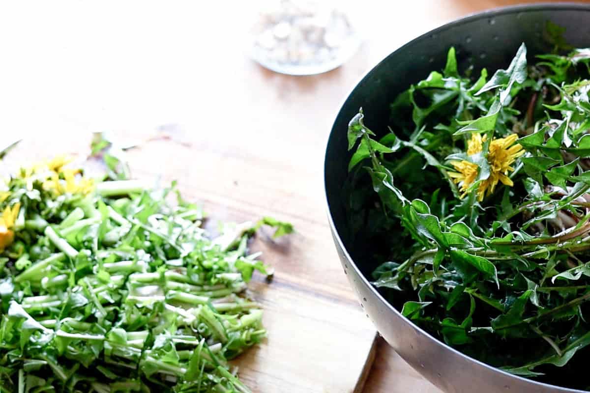 Fresh dandelion roots sliced into thin coins on a wooden cutting board.