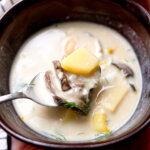 A spoon full of creamy mushroom soup with a mushroom slice, potato chunks, and herbs.