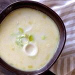 A bowl of creamy potato leek soup with chopped leeks floating on top.