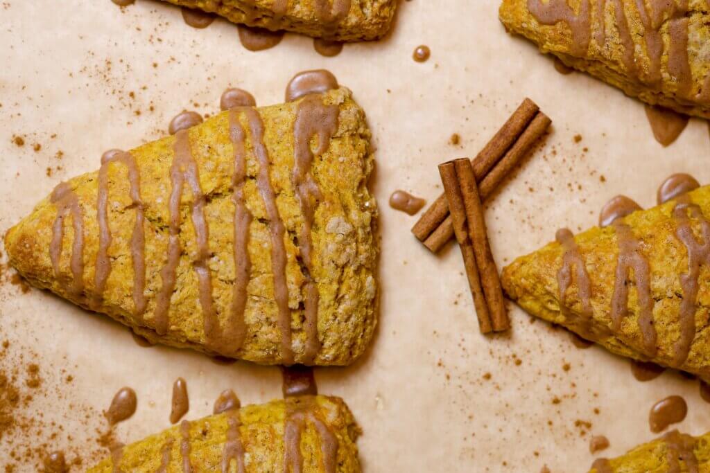a piece of sourdough pumpkin scone drizzled with maple glaze on top and cinnamon on the side